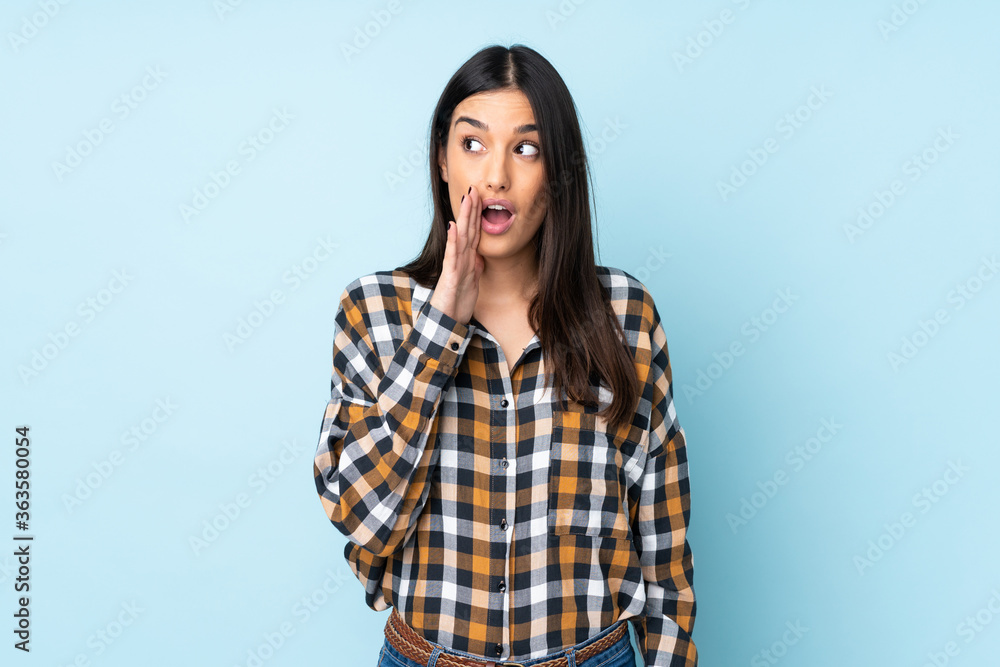 Young caucasian woman isolated on blue background whispering something with surprise gesture while looking to the side Young caucasian woman isolated on blue background whispering something with surprise gesture while looking to the side