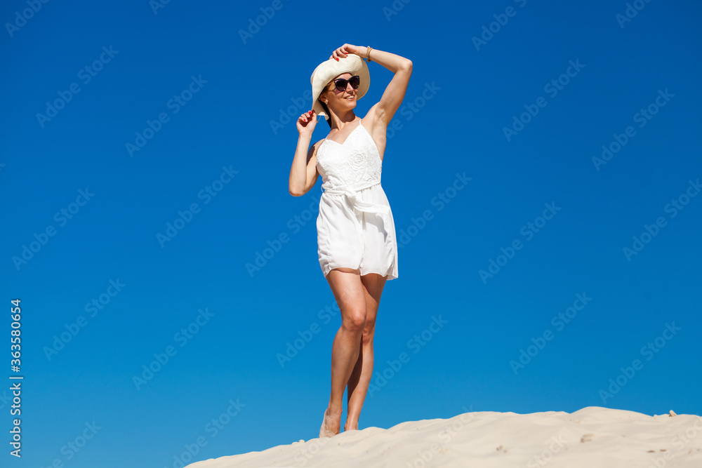 Young beautiful woman in sunglasses and a white dress posing against a blue sky Young beautiful woman in sunglasses and a white dress posing against a blue sky