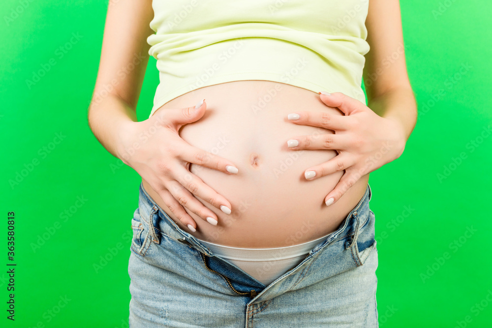 Cropped image of pregnant woman in unzipped jeans showing her baby bump at colorful background with copy space. Waiting for a baby concept Cropped image of pregnant woman in unzipped jeans showing her baby bump at colorful background with copy space. Waiting for a baby concept