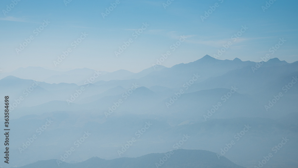 Mountain range silhouette in the mist with blue sky background 