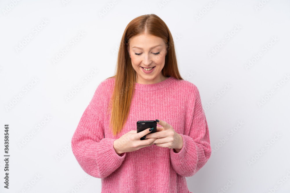Young redhead woman with pink sweater over isolated white background sending a message with the mobile Young redhead woman with pink sweater over isolated white background sending a message with the mobile