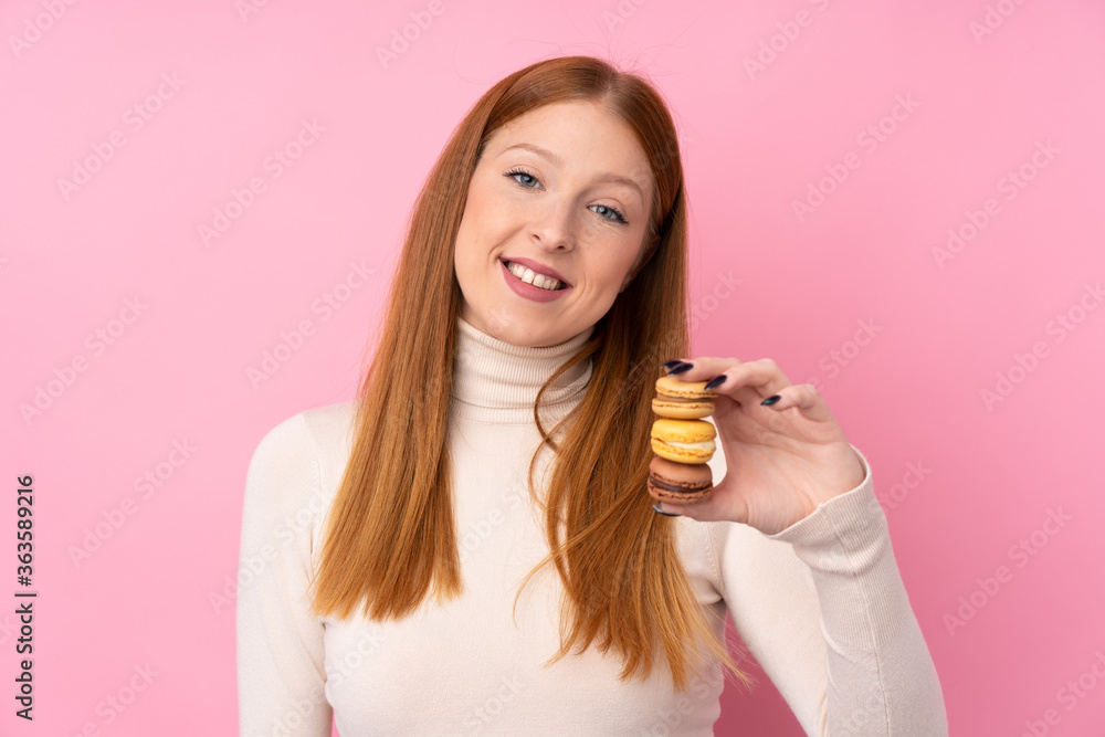 Young redhead woman over isolated pink background holding colorful French macarons and with happy expression Young redhead woman over isolated pink background holding colorful French macarons and with happy expression
