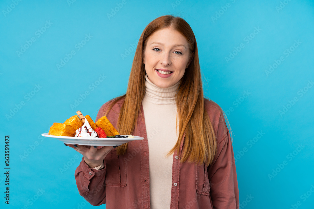 Young redhead woman holding waffles over isolated background smiling a lot Young redhead woman holding waffles over isolated background smiling a lot