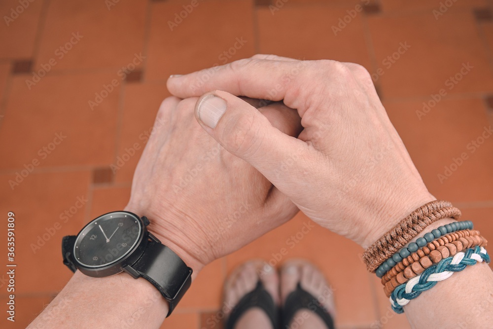 Fototapeta premium Man wearing a bracelet made of rope, wood, leather, beads and colored rope sack. Black watch on man hand. Hipster fashion on tiled flooring background