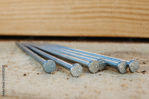 Fasteners and building materials for the roof. A pile of roofing long metal nails lying on pine for roof boards in close-up with a blurry background.