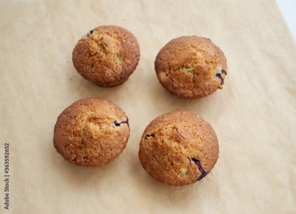 Freshly baked muffins with berries on a light brown crafted parchment, top view. Perfect tasty pastry for breakfasts, snacks, lunch or teatime. Homemade sweets cooking and baking concept. Freshly baked muffins with berries on a light brown crafted parchment, top view. Perfect tasty pastry for breakfasts, snacks, lunch or teatime. Homemade sweets cooking and baking concept.