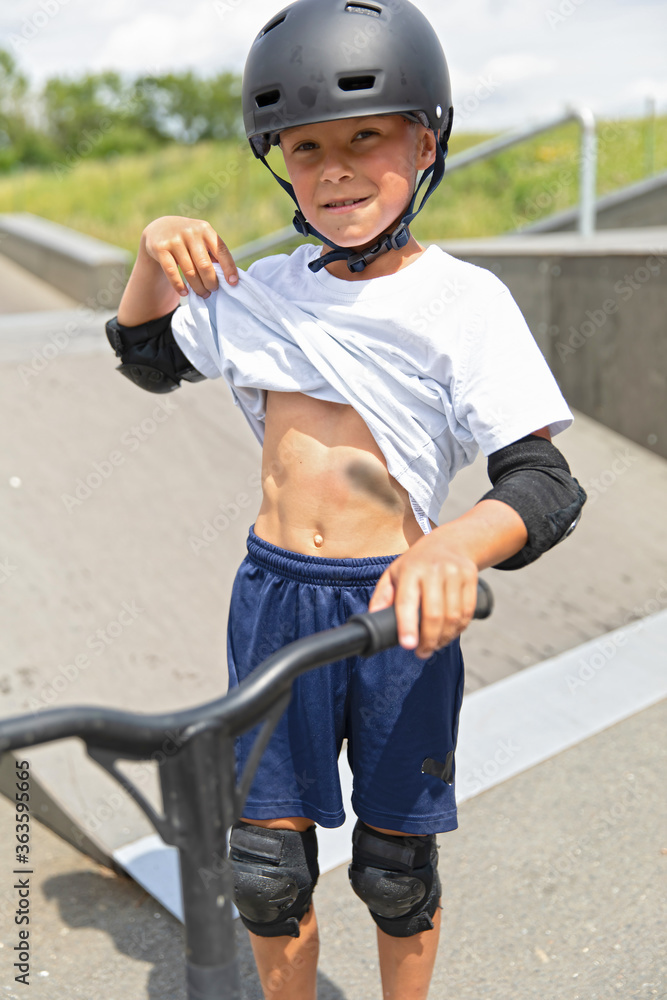 A cute little boy rides a scooter in a skatepark.