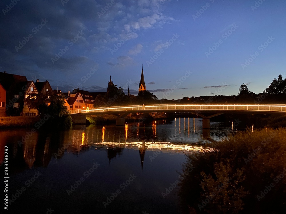 Fototapeta premium Nachtszene mit dunkelblauen Himme, eine beläuchtete Brücke verläuft über dem Fluß und spiegelt sich im Wasser