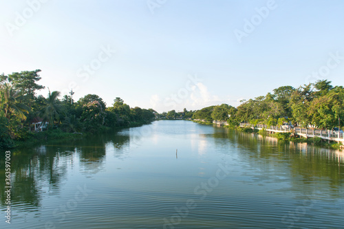 The canal has trees on the other side and a fence.