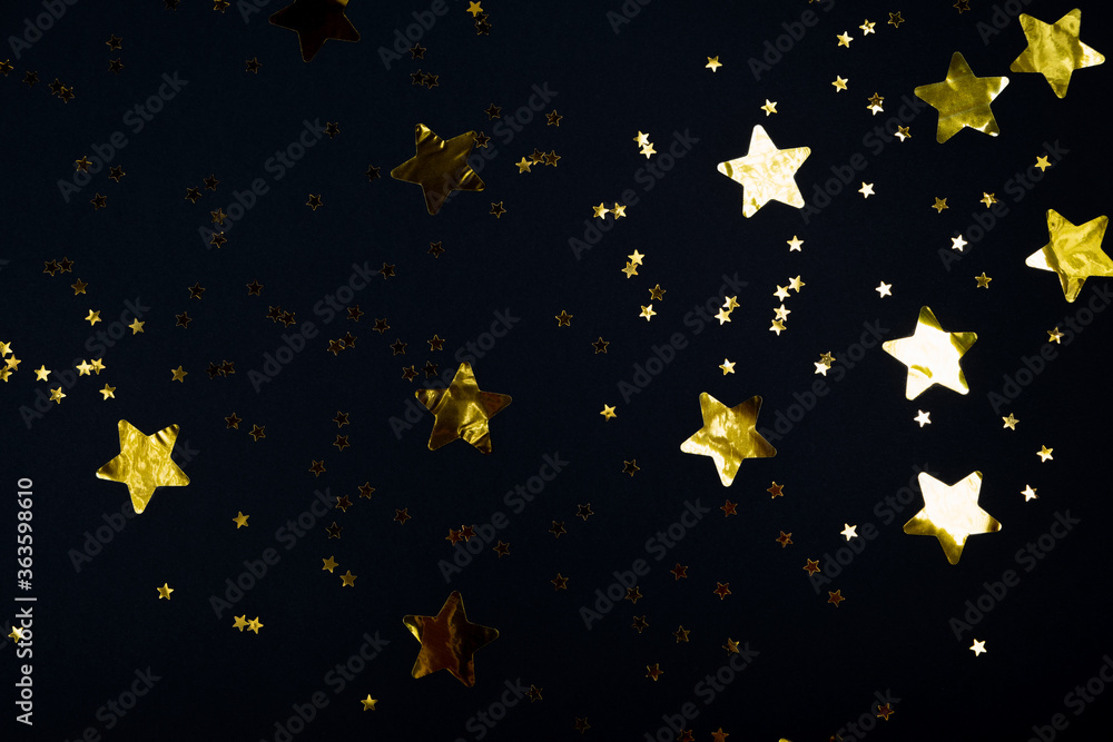 Fototapeta premium Black contrast color festive background with golden stars glitter confetti. Flat lay style with copy space for text, design. Trendy Holiday concept. Perfect backdrop for social media, blog, postcard