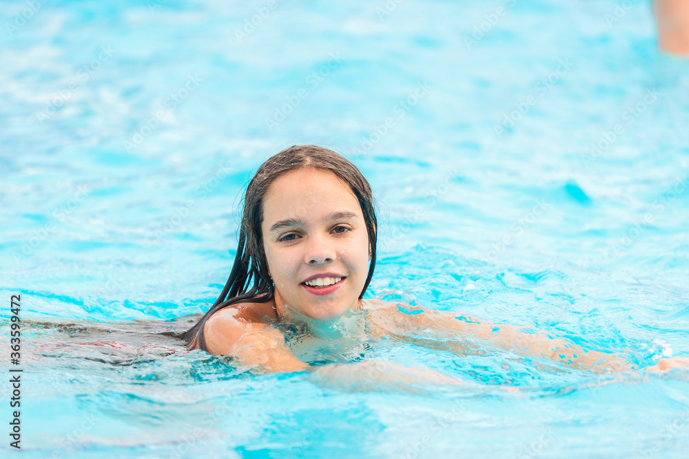 Teenage girl swims in the clear blue water of a pool during a vacation in a warm tropical country on a sunny warm summer day. Travel concept. Advertising space