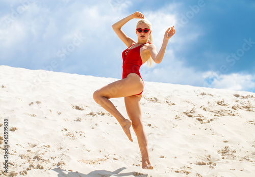 Young beautiful blonde woman in a solid red swimsuit posing on the beach