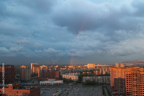 View from the balcony of a multi-storey building to a new building area against a dark blue sky after a thunderstorm and rainbow. Urban jungle in the orange rays of the setting sun.