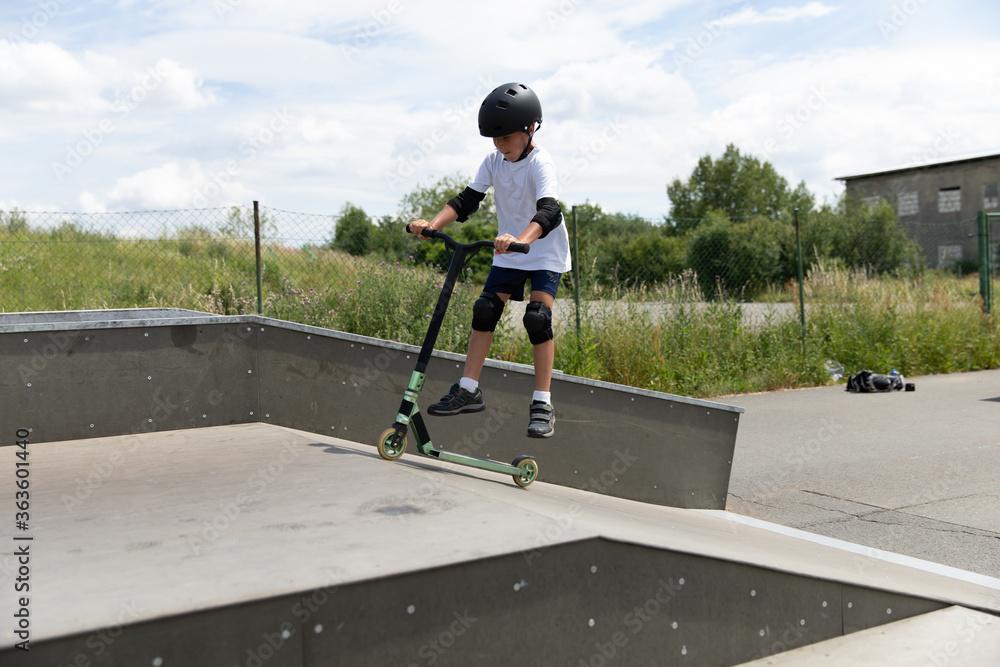 The boy jumps on a scooter.