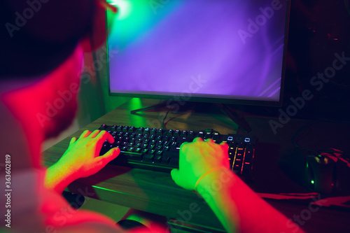 Cyber sport. Copyspace on monitor, screen. Fully concentrated professional gamer playing important match. Caucasian man practicing before tournament alone in neon light. E-sport, gamer, streamer.