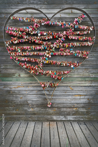 A wooden wall with a metal heart and colorful padlocks hung on it. Symbols of unbroken relationship and love.
