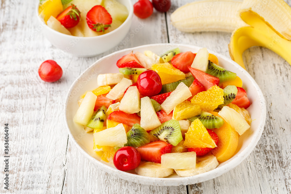 Fruit salad in a plate of chopped strawberries, kiwi, banana, orange and cherry on white wooden background. Healthy organic food.