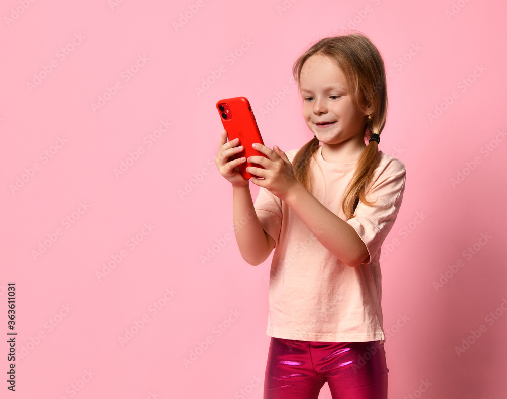 Portrait of a smiling casual girl holding smartphone over pink background Portrait of a smiling casual girl holding smartphone over pink background