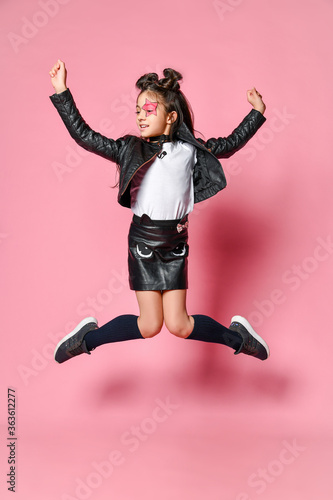 fashionable hipster punk girl - dressed in a leather jacket and skirt, black knee-highs and a white t-shirt, leaps high on a pink