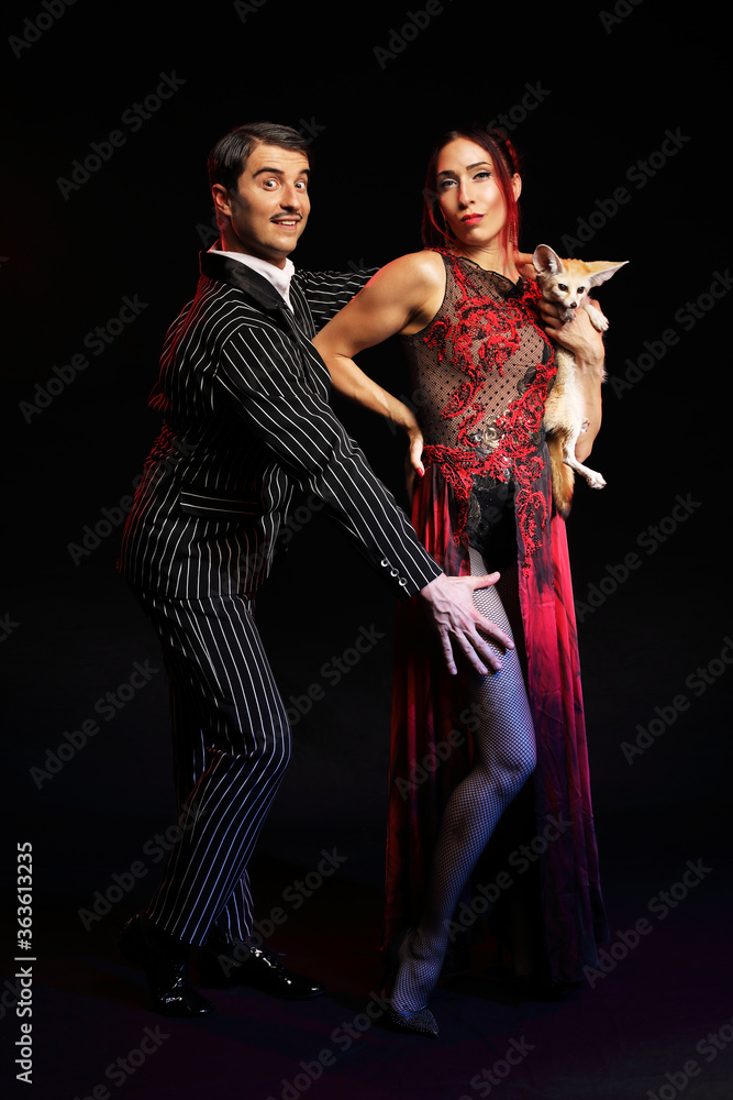 Fanny man with mustache in suit and sexy woman in luxury evening dress holding wild fox isolated on black background