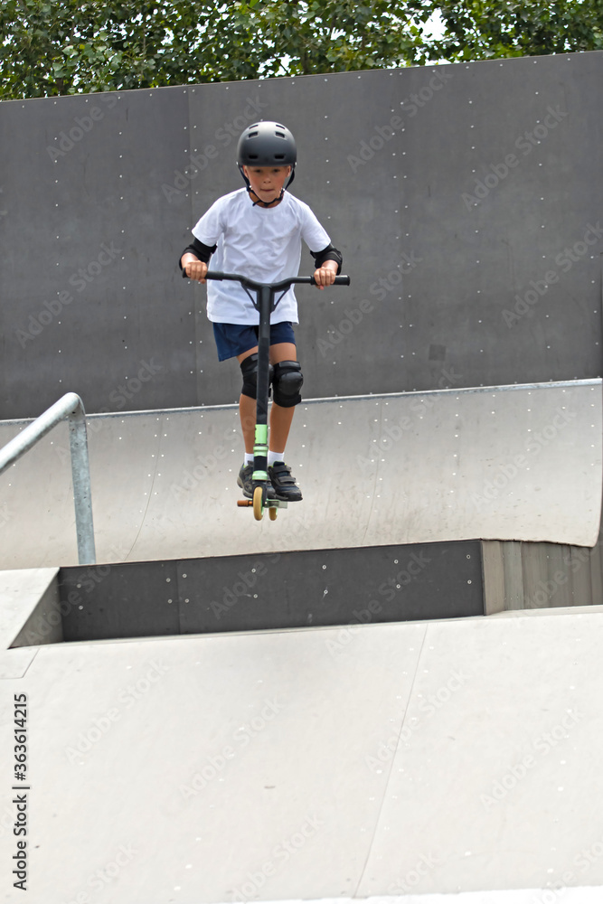The boy jumps on a scooter.