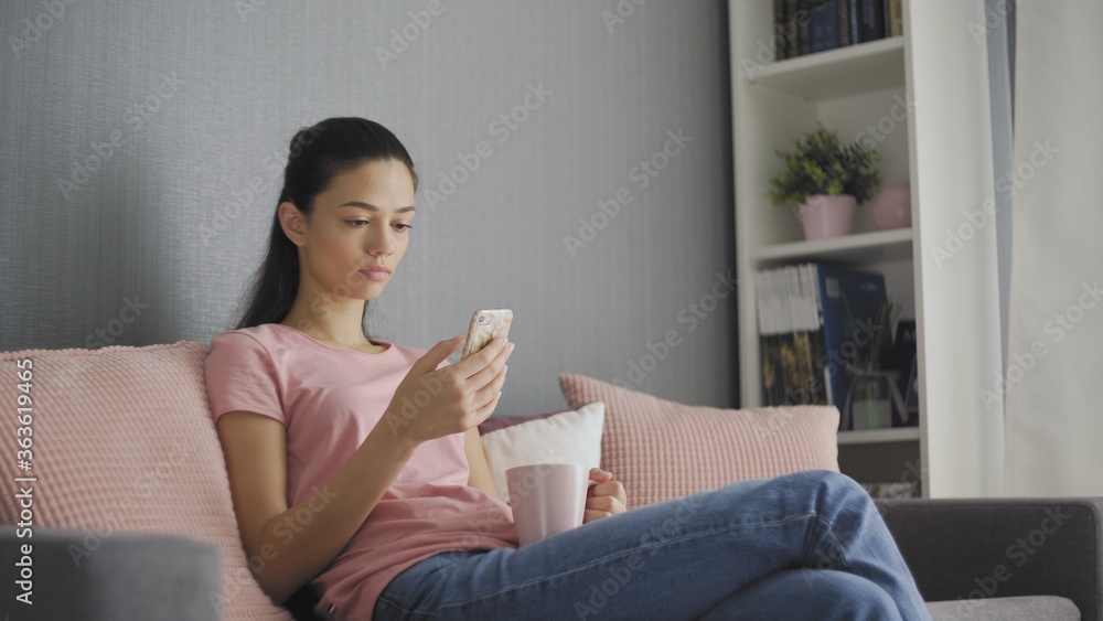 beautiful young woman using smartphone relaxing on couch at home browsing online texting drinking coffee enjoying comfortable lifestyle beautiful young woman using smartphone relaxing on couch at home browsing online texting drinking coffee enjoying comfortable lifestyle
