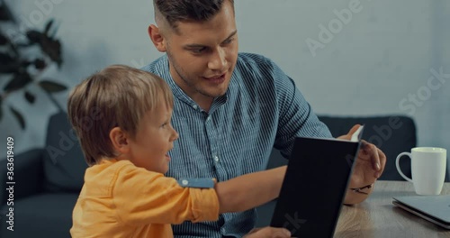 cheerful father showing notebook to cute son at home photo