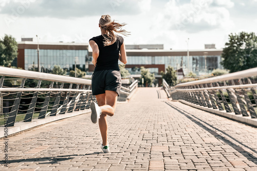 Young woman jogging. A girl runs over a bridge in the city early in the morning.