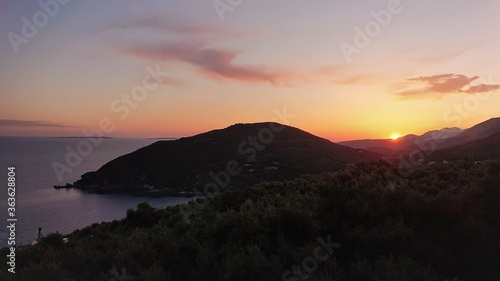 sunset over the sea with silhouette of a hill and olive trees 