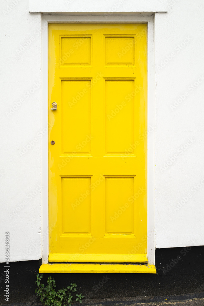 Simple design wooden yellow front door to a residential home property The surrounding wall is white with a black base.