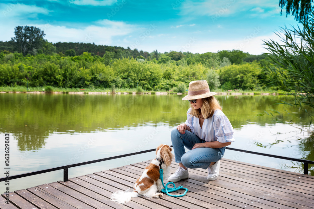 Mature woman and her puppy relaxing together on the pier by the lake Mature woman and her puppy relaxing together on the pier by the lake