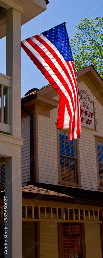 The American Flag brightly highlighted by the sun as it proudly waves between two buildings in a rural town 