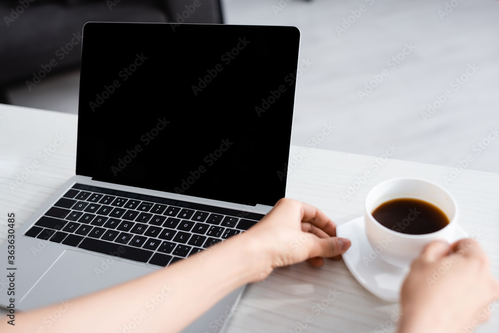 Cropped view of woman hands holding cup of coffee and laptop Cropped view of woman hands holding cup of coffee and laptop