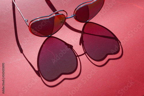 Beautiful shadow. Light passes through from heart-shaped glasses on pink background. Sun hard light shadow reflection. Free space for text. Summer concept.