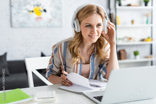 Selective focus of attractive woman in headphones looking at laptop while studying online photo
