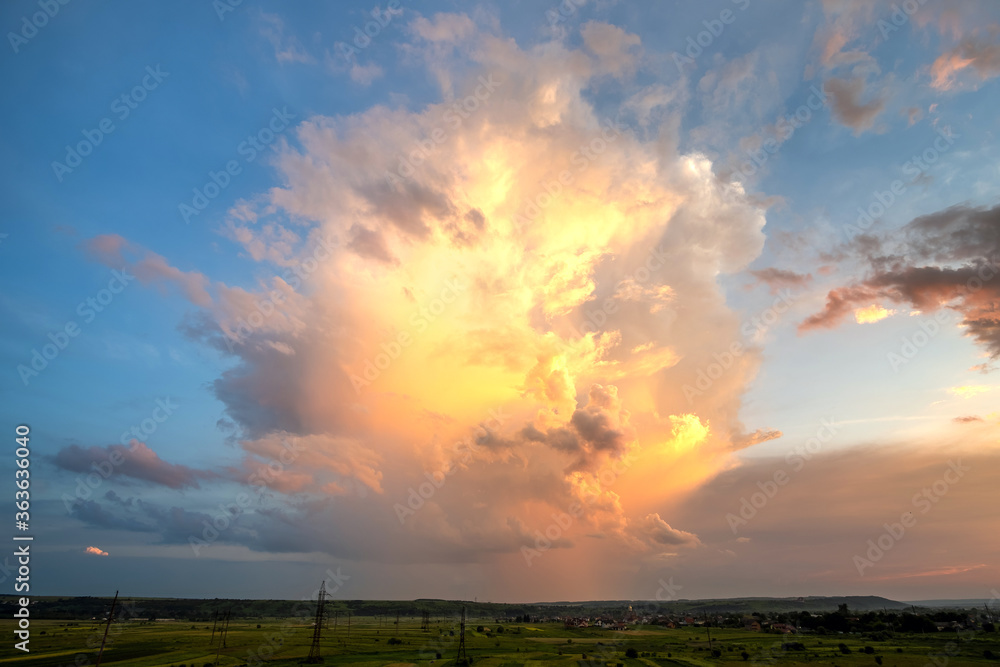 Dramatic yellow sunset over rural area with stormy puffy clouds lit by orange setting sun and blue sky.