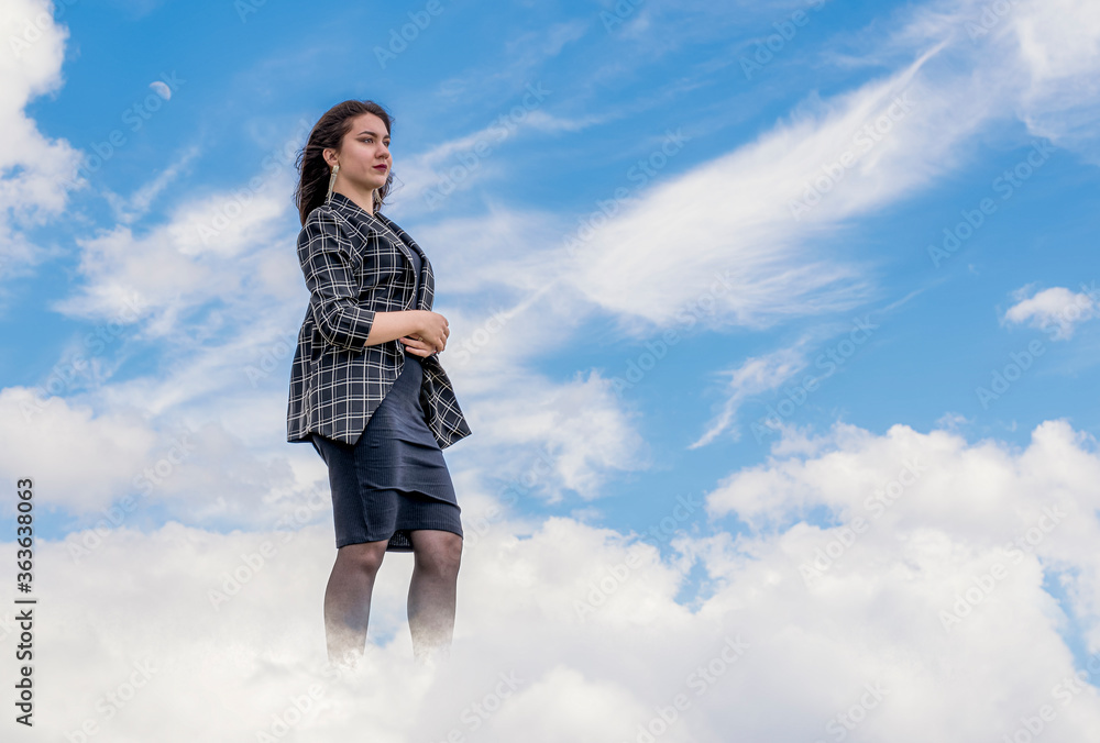 A young girl slowly walks through the clouds in a dark dress and a checkered jacket on a background of blue sky A young girl slowly walks through the clouds in a dark dress and a checkered jacket on a background of blue sky