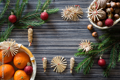 Christmas background (template) with new year balls, handmade straw ornaments, tangerines, spruce branches and sweets on a dark wooden textured surface. View from above.