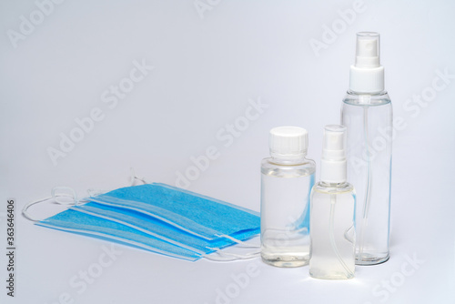 bottle of lotion, sanitizer or liquid soap and protective mask over light grey background