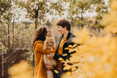 Young couple with a red cat on a background of an autumn park.