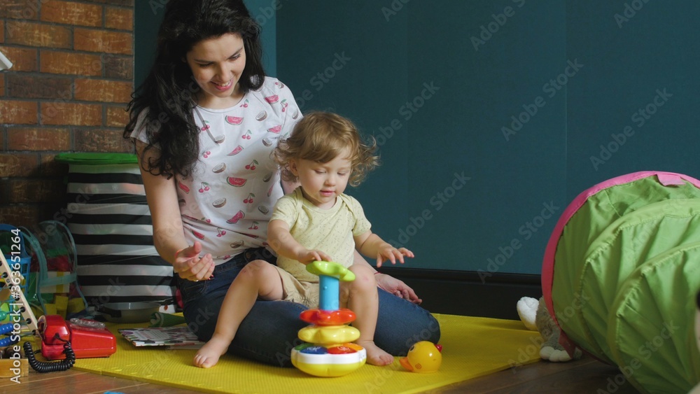Fototapeta premium Mother and daughter playing with children's pyramid on the floor