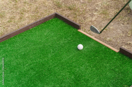 Golf sport game with niblick and white ball on the green grass. Playing in mini-golf. Empty place for advert right side.