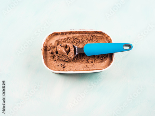 Ice cream scoop in chocolate ice cream tub on green turquoise background. Closeup