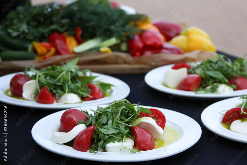 Italian cuisine. Caprese with arugula in a white plate on a black table. Fresh vegetables, catering. Banquet, table setting. Background image, copy space