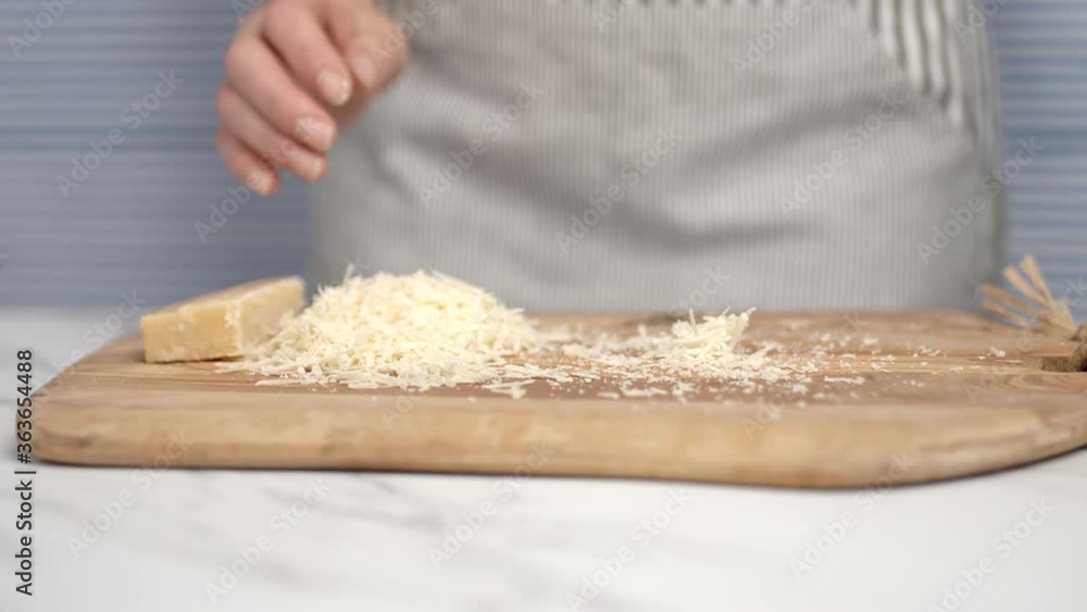 Close-up of female hands grating parmesan cheese. Shredding cheese with a cheese grater. Close-up of female hands grating parmesan cheese. Shredding cheese with a cheese grater.