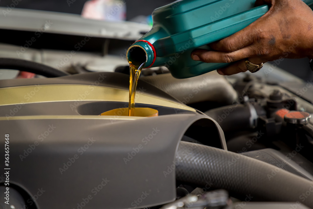 Car mechanic replacing and pouring fresh oil into engine at maintenance repair service station, Mechanic pouring oil into car at the repair garage. Fresh oil being poured during an oil change to a car