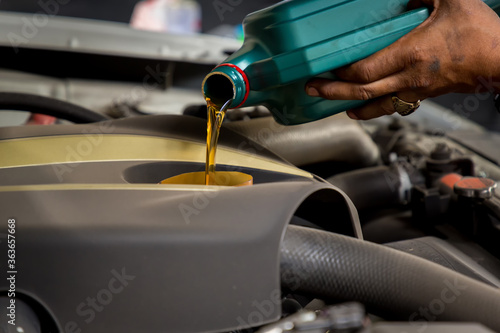 Car mechanic replacing and pouring fresh oil into engine at maintenance repair service station, Mechanic pouring oil into car at the repair garage. Fresh oil being poured during an oil change to a car © kanpisut