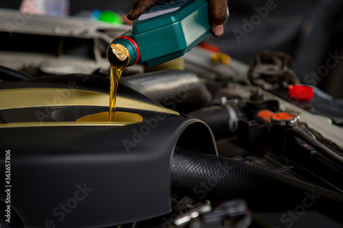 Car mechanic replacing and pouring fresh oil into engine at maintenance repair service station, Mechanic pouring oil into car at the repair garage. Fresh oil being poured during an oil change to a car © kanpisut