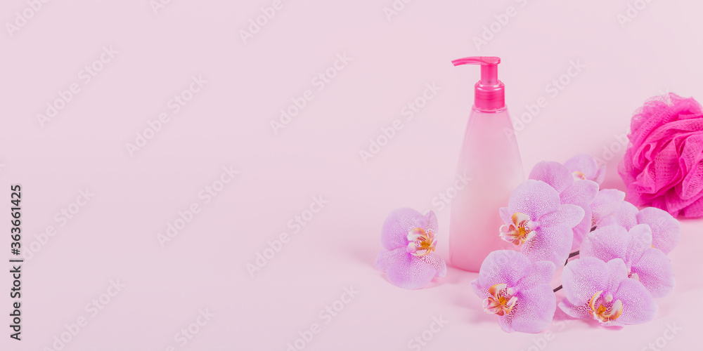 Plastic dispenser bottle with cosmetic soap, shampoo or shower gel, pink sponge and purple orchid flowers on pink background. Spa and wellness concept Plastic dispenser bottle with cosmetic soap, shampoo or shower gel, pink sponge and purple orchid flowers on pink background. Spa and wellness concept