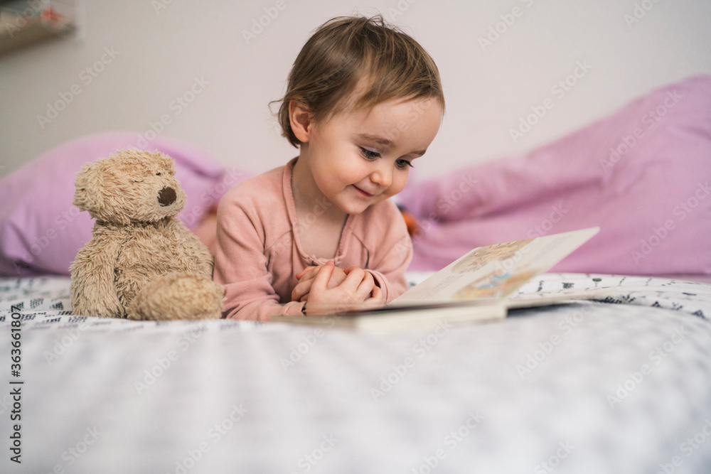 Adorable toddler girl lying on bed watching book Adorable toddler girl lying on bed watching book
